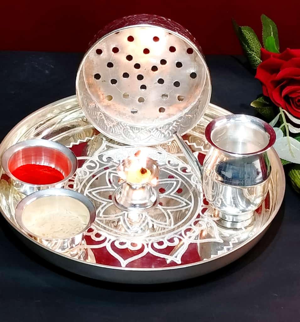 Decorative silver tray with lit candle, small bowls, and a rose on a dark background